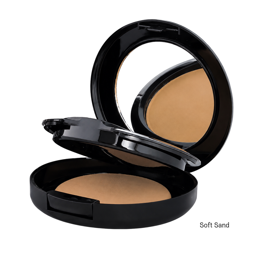 An open black round compact powder foundation with a mirror on the inside lid, showing a light tan pressed powder labeled 'Soft Sand' on a white background.