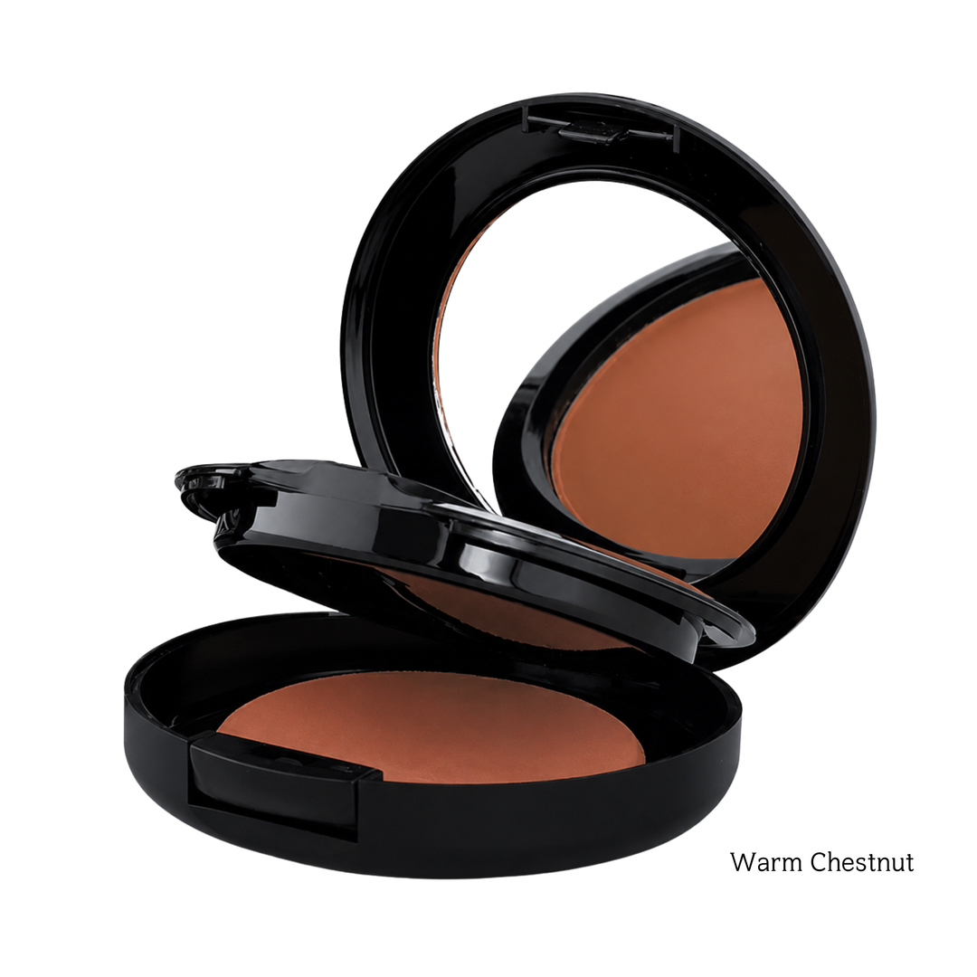 An open black makeup compact showing a warm chestnut brown foundation powder, with the mirror visible in the lid and the text 'Warm Chestnut' in the bottom right corner.