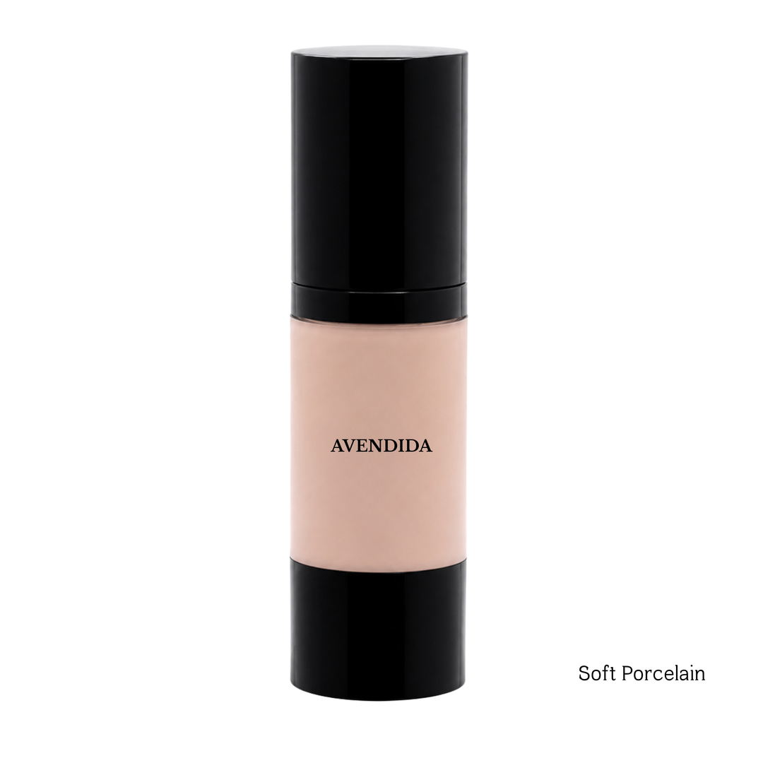 A bottle of AVENDIDA liquid foundation in the shade Soft Porcelain, featuring a light peach-beige liquid visible through a clear bottle with black caps, set against a plain white background.