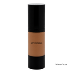 Load image into Gallery viewer, A bottle of AVENDIDA liquid foundation in the shade Warm Cocoa, featuring a warm brown liquid visible through a clear cylindrical bottle with a glossy black cap and base, set against a plain white background.