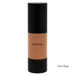 Load image into Gallery viewer, A bottle of AVENDIDA liquid foundation in the shade Warm Beige, featuring a black cap and base with the beige makeup visible through the clear center bottle, on a white background.