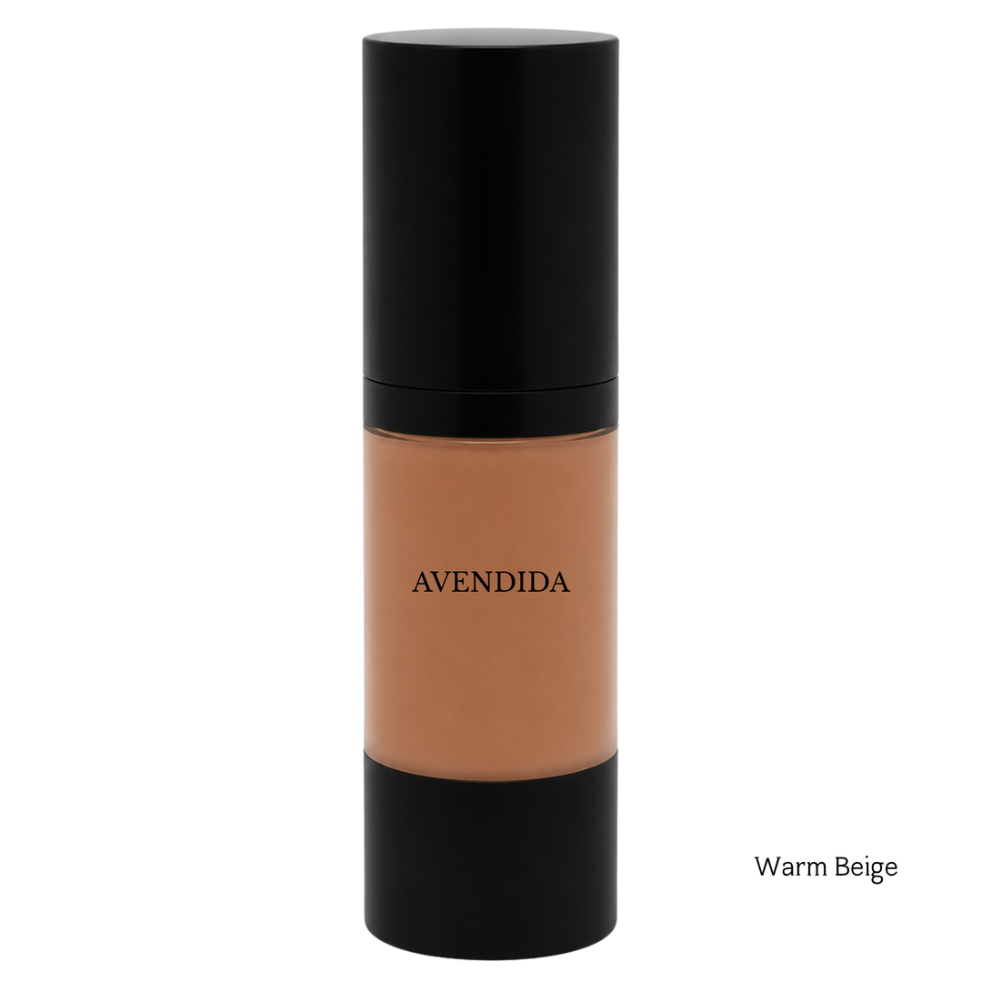 A bottle of AVENDIDA liquid foundation in the shade Warm Beige, featuring a black cap and base with the beige makeup visible through the clear center bottle, on a white background.